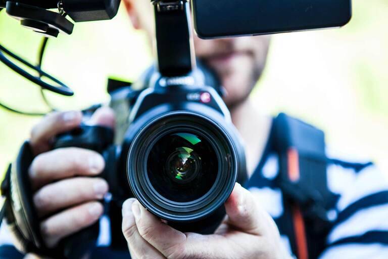 SIMONSAYS DIGITAL AGENCY DSLR camera held by a person in a striped shirt, capturing vibrant outdoor scenes.