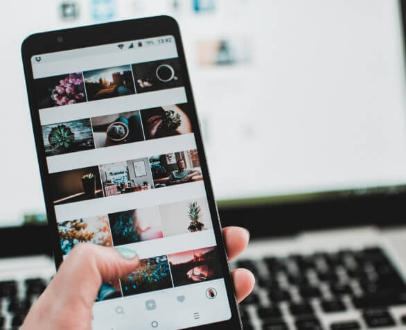 SIMONSAYS DIGITAL AGENCY Instagram interface displayed on a smartphone, showing a grid of various images while a laptop is in the background.