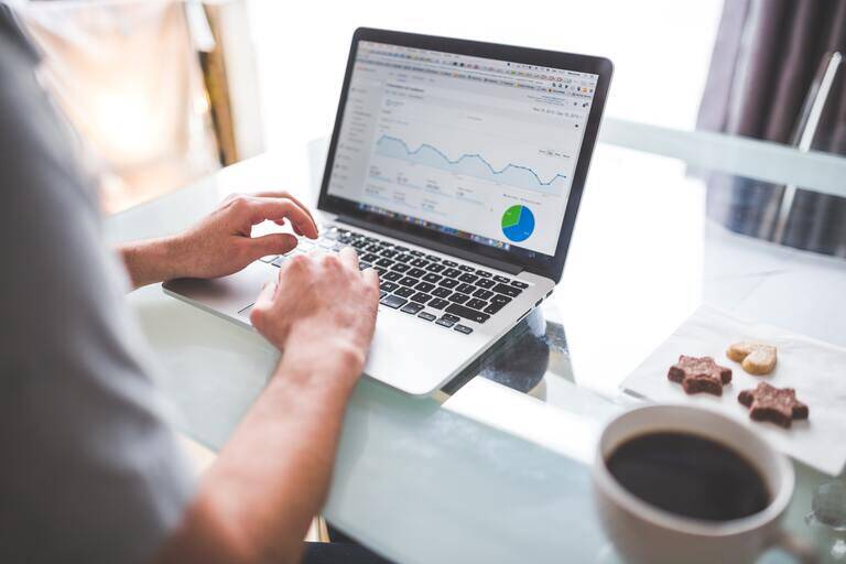 SIMONSAYS DIGITAL AGENCY Workspace with laptop displaying analytics data, cup of coffee, and snacks on a glass table.