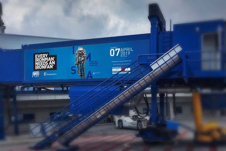 SIMONSAYS DIGITAL AGENCY Standard Bank advertisement for Ironman event featuring a cyclist, date, and distance details.